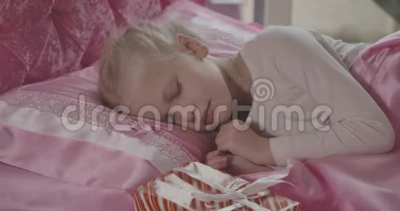 可爱的金发白种人女孩的肖像她的辫子早上醒来在粉红色的枕头上发现圣诞礼物视频的预览图
