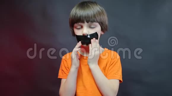 一个穿橙色T恤的孩子从脸上剥下一条黑色胶带视频的预览图