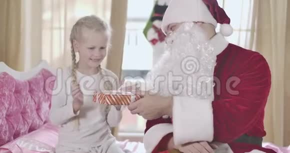 可爱的金发白种人女孩的肖像扎着辫子当圣诞老人送她圣诞礼物时她搓着手儿童视频的预览图