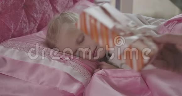睡在粉红色床上的漂亮白人女孩的特写肖像就像男人把圣诞礼物放在枕头上一样视频的预览图