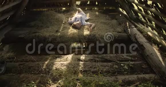 年轻女子在阳光下微笑晒在干草上木制棚子4K视频的预览图