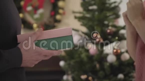 特写白种人的女性手拿礼物盒在圣诞树前打开它扔回来女孩视频的预览图
