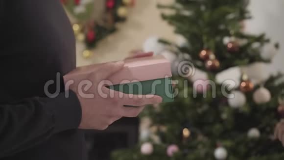 镜头跟随男性高加索人手上的礼物盒送给一个无法辨认的年轻女孩微笑的女人迎接圣诞节视频的预览图