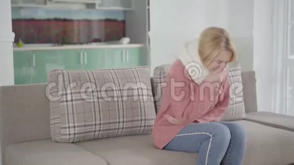 白人妇女戴着白色围巾坐在沙发上咳嗽的肖像年轻人拿着一杯热饮料来疾病视频的预览图