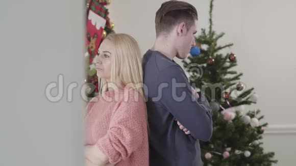 在圣诞花环和新年树的背景下一对痛苦的白种人夫妇背靠背站着的画像视频的预览图