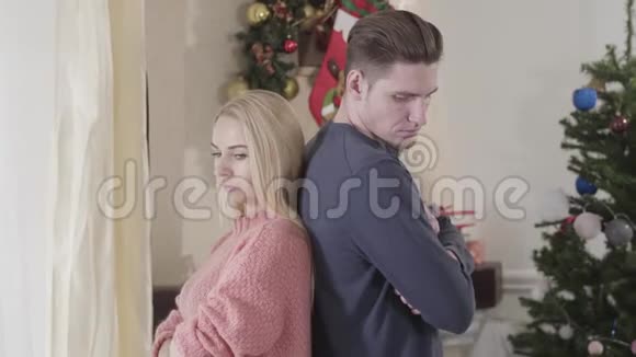 镜头慢慢接近悲伤的白种人夫妇背靠背地站在圣诞花环和新花的背景下视频的预览图