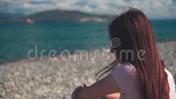 在海滩上坐着粉色t恤的年轻女子或女孩的正面视角远比镜头远女孩试图视频的预览图