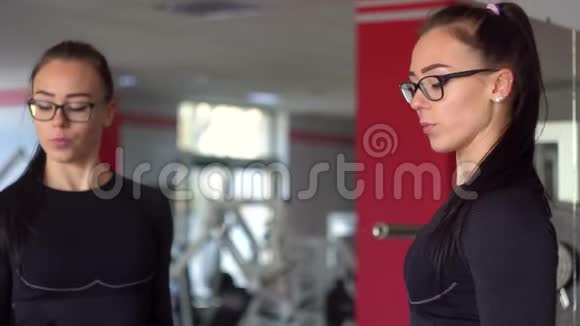 年轻的健身妇女在健身房用蓝色哑铃锻炼体育俱乐部戴眼镜的漂亮女孩视频的预览图