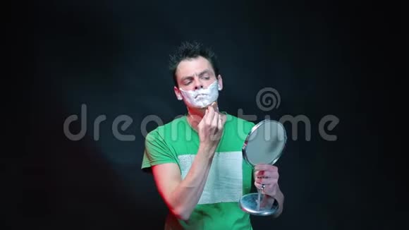 一个穿绿色T恤的人在刮胡子手里拿着镜子视频的预览图