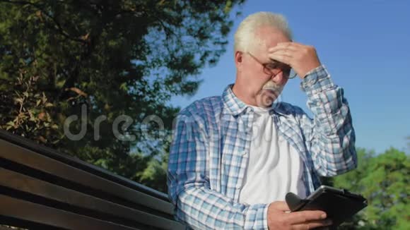 一位留着胡子的老人正在看书一个老人很热他用手擦脸视频的预览图