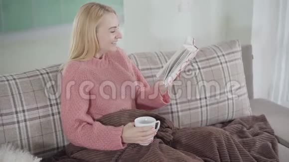 镜头接近笑白种人女人在家看书美丽的女人坐着小说和热辣的杯子视频的预览图