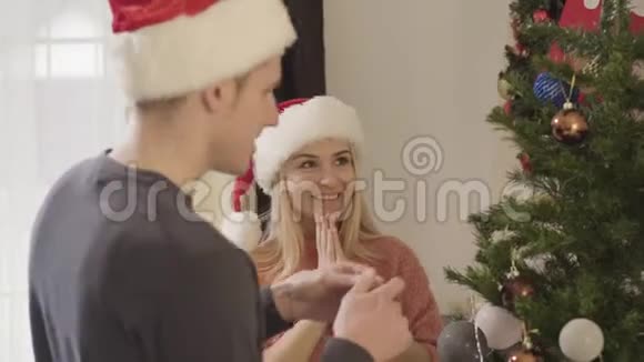 年轻的白种人男人把最后的装饰挂在圣诞树上他兴奋的妻子拥抱着可爱的丈夫快乐的人视频的预览图