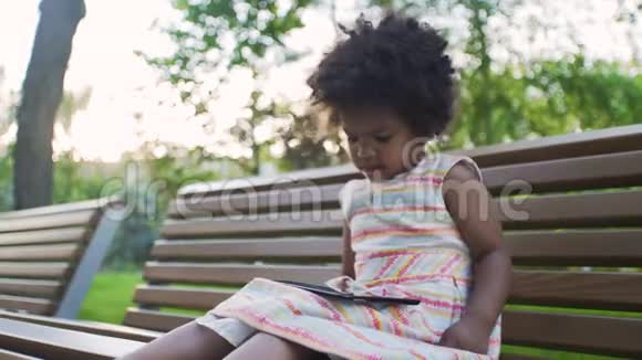 不高兴的非裔美国女孩正在公园的平板电脑上看动画片视频的预览图