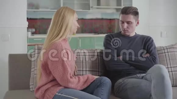 一对不高兴的白人夫妇坐在家里的沙发上的肖像年轻男子双手交叉美丽的女人视频的预览图