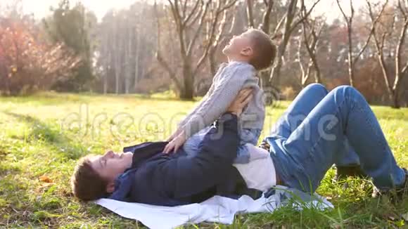 一个年轻的父亲和一个孩子玩把它抱在怀里太阳光线穿透树木欢笑和欢乐视频的预览图