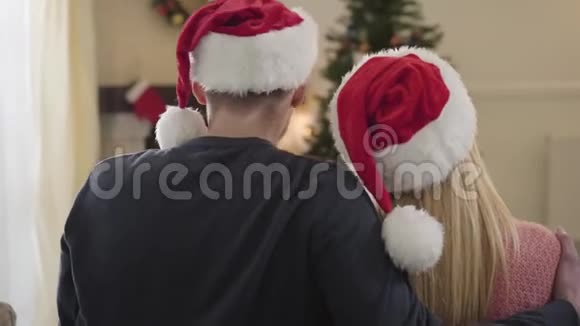在圣诞树前拥抱白人夫妇的后景戴红帽子的积极家庭视频的预览图