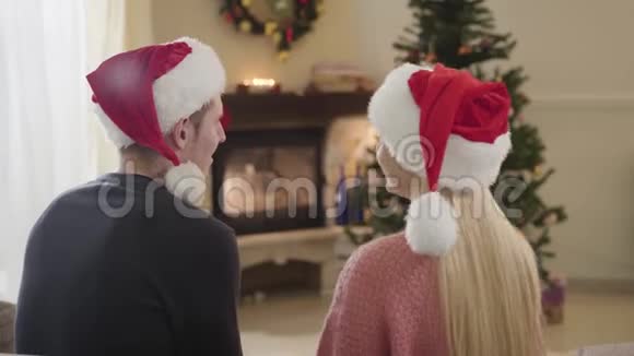 正面的白人夫妇笑得像坐在圣诞树前女人和男人在红色的圣诞节视频的预览图