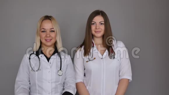 两个穿着灰色背景的白色医疗外套的女医生保健概念视频的预览图