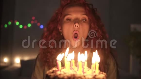 一个微笑的卷曲的红头发女孩许愿并在她的生日蛋糕上吹蜡烛的肖像粉碎的光视频的预览图