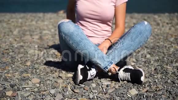 穿着粉红色T恤和蓝色牛仔裤的漂亮女孩或坐在海滩上使用智能手机的女人视频的预览图