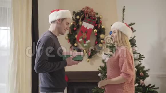 戴着红色圣诞帽的白种人年轻女子侧视着丈夫送给她的礼物视频的预览图