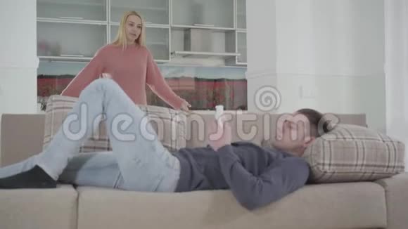 一位年轻漂亮的高加索女人抱怨家庭问题而她的丈夫躺在沙发上用视频的预览图