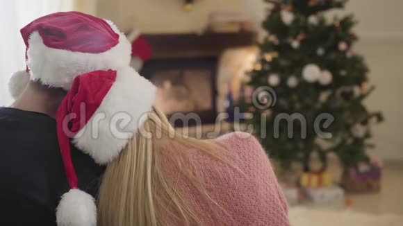 镜头慢慢地接近坐在新年树前戴着红色圣诞帽的年轻夫妇幸福配偶视频的预览图