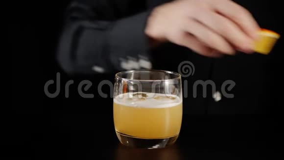 威士忌酸鸡尾酒酒保拿了一片橘子放在一个带有威士忌酸鸡尾酒的石头玻璃里装饰视频的预览图