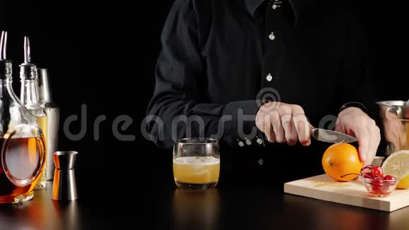 威士忌酸鸡尾酒酒保拿着一把刀把一个橙色多汁的橘子切成两半放在木板上橙色滴片视频的预览图