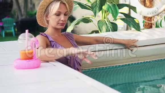 年轻的美女正在游泳池里放松喝果汁视频的预览图