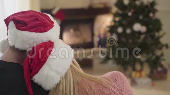 镜头从一对戴着红色圣诞帽的年轻夫妇转移到新年树前家庭幸福平静视频的预览图