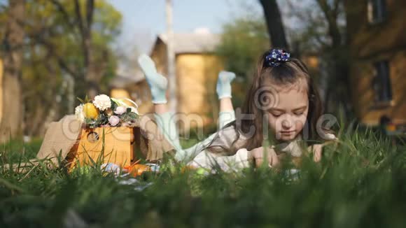 一个7岁或8岁的女孩手臂挽着一篮子复活节兔子躺在房子附近的草地上视频的预览图