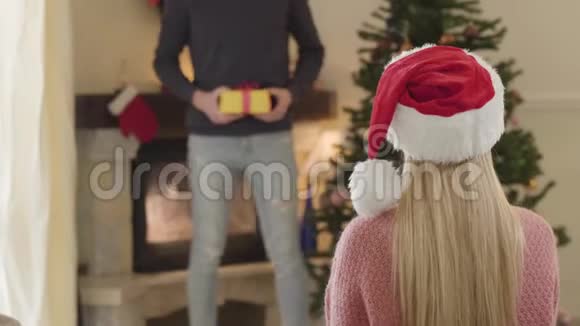 模糊的白种人男人在后台拿着礼品盒作为金发女人在前面等待礼物幸福家庭视频的预览图