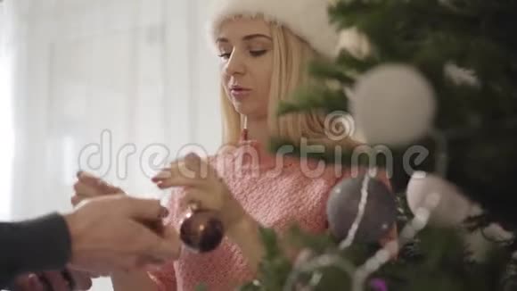 一幅美丽的白种人女人帮助无法辨认的男人在圣诞树上挂装饰品的肖像幸福的妻子视频的预览图