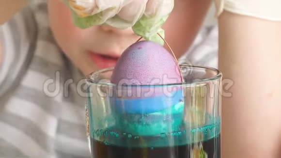 特写孩子用一只手拿着一个鸡蛋把它扔进一杯油漆里视频的预览图