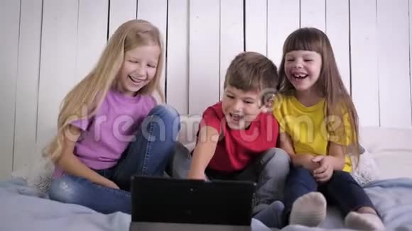 快乐的童年快乐的孩子们在数码平板电脑上看有趣的视频在放松的时候坐在床上大笑视频的预览图