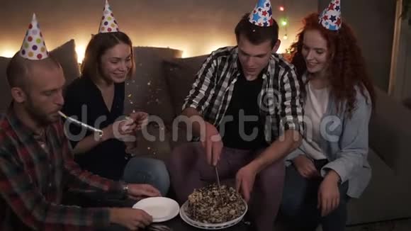 穿格子衬衫的生日人用五颜六色的锥形帽子剪生日蛋糕在圆锥体中快乐的朋友视频的预览图