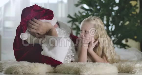 可爱的白种人女孩金发卷发躺在圣诞老人的背景下微笑漂亮的孩子视频的预览图