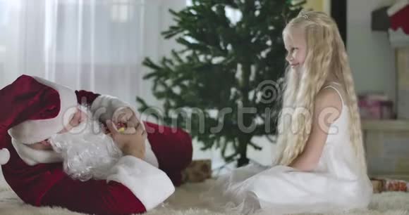 穿着圣诞老人服装的白人男子拿着圣诞礼物和坐在前面的可爱女孩交谈视频的预览图