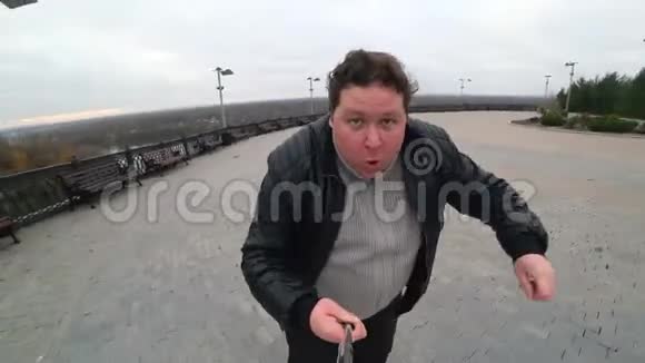 城里跑的胖子男人用自拍棒在动作相机上拍摄自己广角镜头视频的预览图