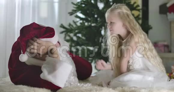 积极的白人女孩金色卷发做安静的手势并与圣诞老人在家交谈儿童圣诞节视频的预览图