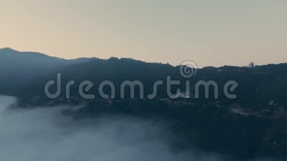 从鸟瞰云层的角度无人机拍摄了一片茂密的森林和一条蜿蜒的雾路群山视频的预览图