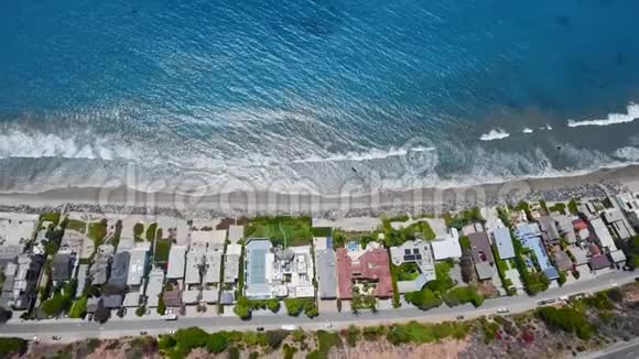 空中拍摄的房屋和海滩蓝色海洋和白色海浪的画面视频的预览图