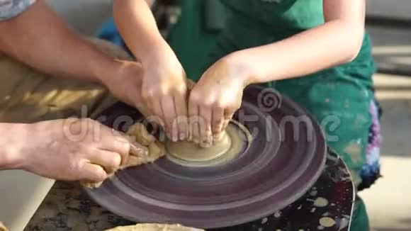 孩子们的手在黄色的粘土上旋转着陶工轮塑造了盘子师父和弟子视频的预览图