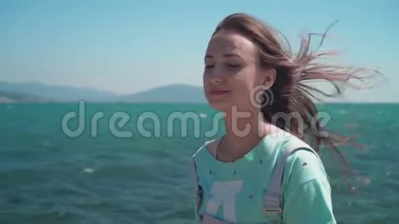 海岸上一个穿蓝色T恤的女孩的肖像少女背景上的海山和天视频的预览图