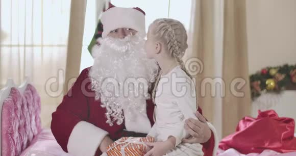 穿圣诞老人服装的白种人成年男子假胡子抱着可爱的女孩跪在地上的肖像小孩告诉他视频的预览图