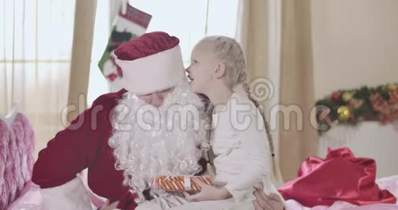 开朗的金发白种人女孩坐在圣诞老人的膝盖上在他的耳边低语戴着辫子的漂亮孩子视频的预览图