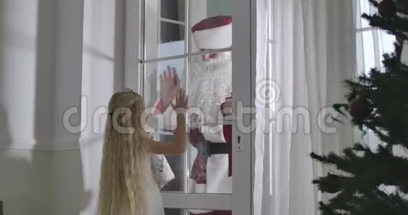 可爱的白人女孩金发向圣诞老人挥手男人离开孩子坐下来带着圣诞礼物童年视频的预览图