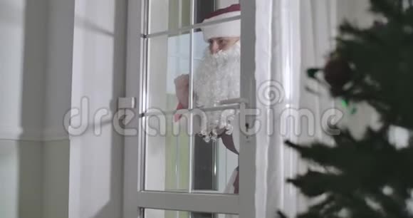 圣诞老人站在玻璃门后面像可爱的孩子一样挥手跑起来向后挥手微笑的男人视频的预览图
