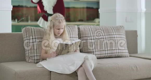 白人女孩穿着优雅的白色连衣裙和皇冠坐在马车上读着圣诞老人的画像视频的预览图